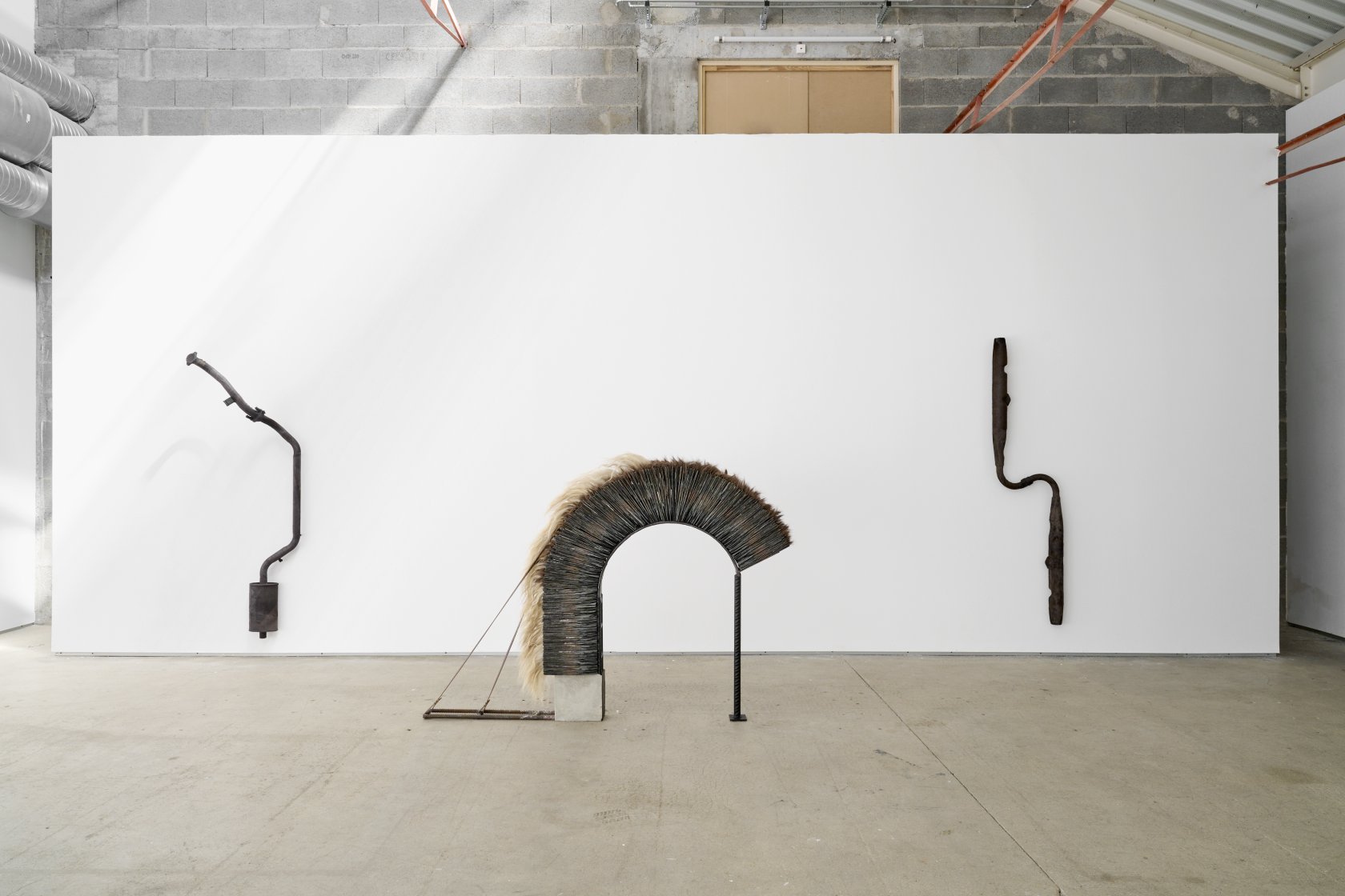 Lucille Jallot, *Caryatides*, pots d’échappements, cuir, 2022 ; *Demi-volte*, ardoise, acier, béton, poils de chèvre, cuir, 2022. Vue de l’exposition *Tendres combustions*, Le confort moderne, Poitiers, 2022. © Pierre Antoine